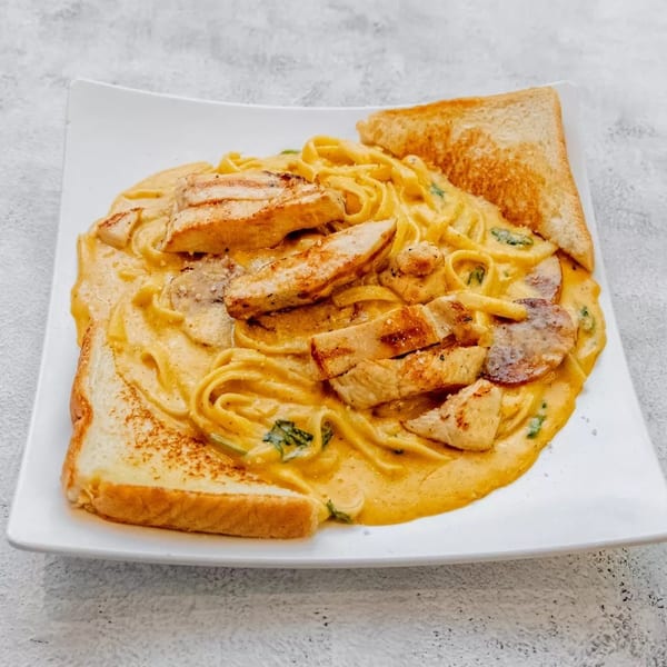 Creamy fettuccine pasta with grilled chicken, sausage, spinach, and two slices of toast.