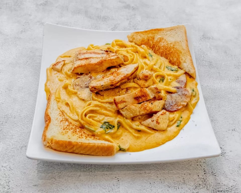 Creamy fettuccine pasta with grilled chicken, sausage, spinach, and two slices of toast.