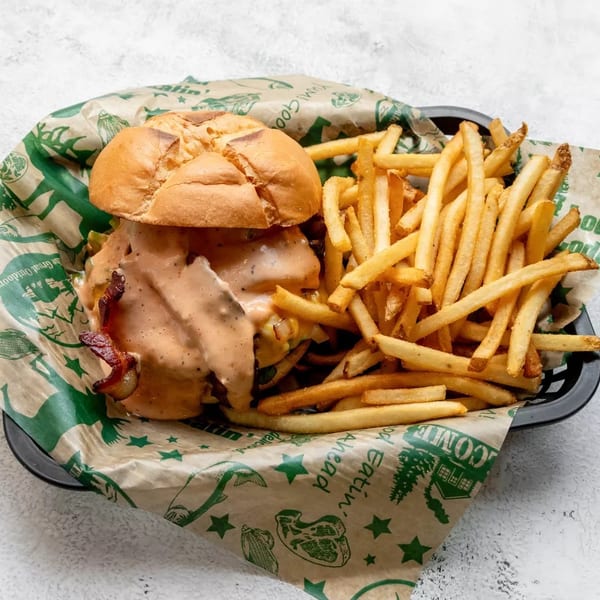 A burger with sauce and bacon, served with a side of fries in a basket.