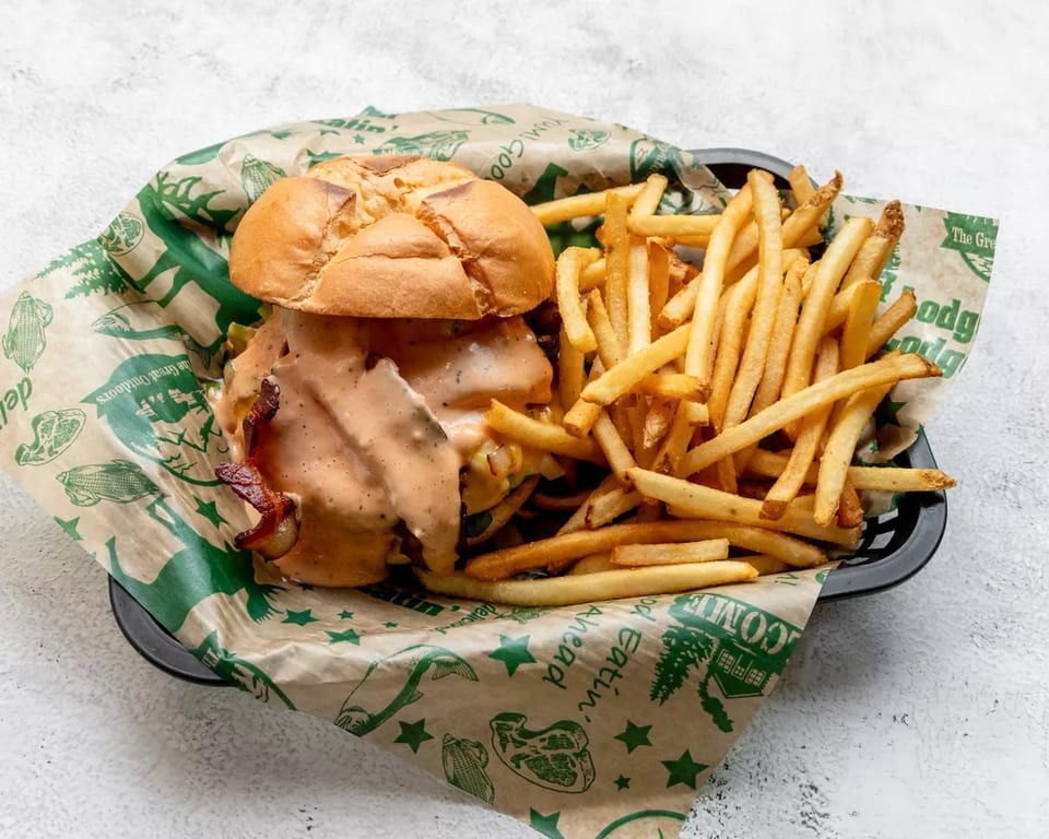 A burger with sauce and bacon, served with a side of fries in a basket.
