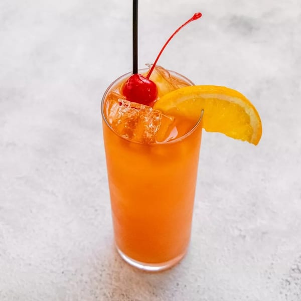 Orange cocktail with ice, garnished with a cherry, orange slice, and black straw.