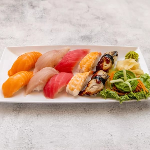 A white rectangular plate holds a variety of sushi, including salmon, tuna, shrimp, and eel nigiri.