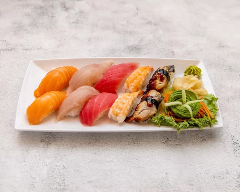 A white rectangular plate holds a variety of sushi, including salmon, tuna, shrimp, and eel nigiri.