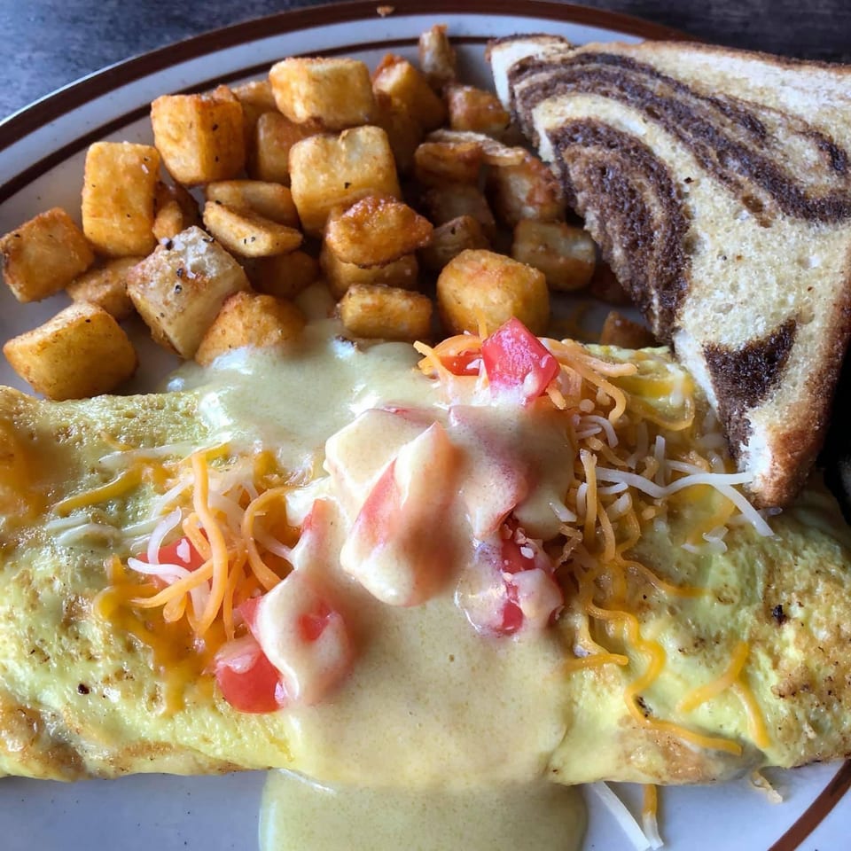 A breakfast plate with an omelet topped with cheese and tomatoes, home fries, and marble rye toast.