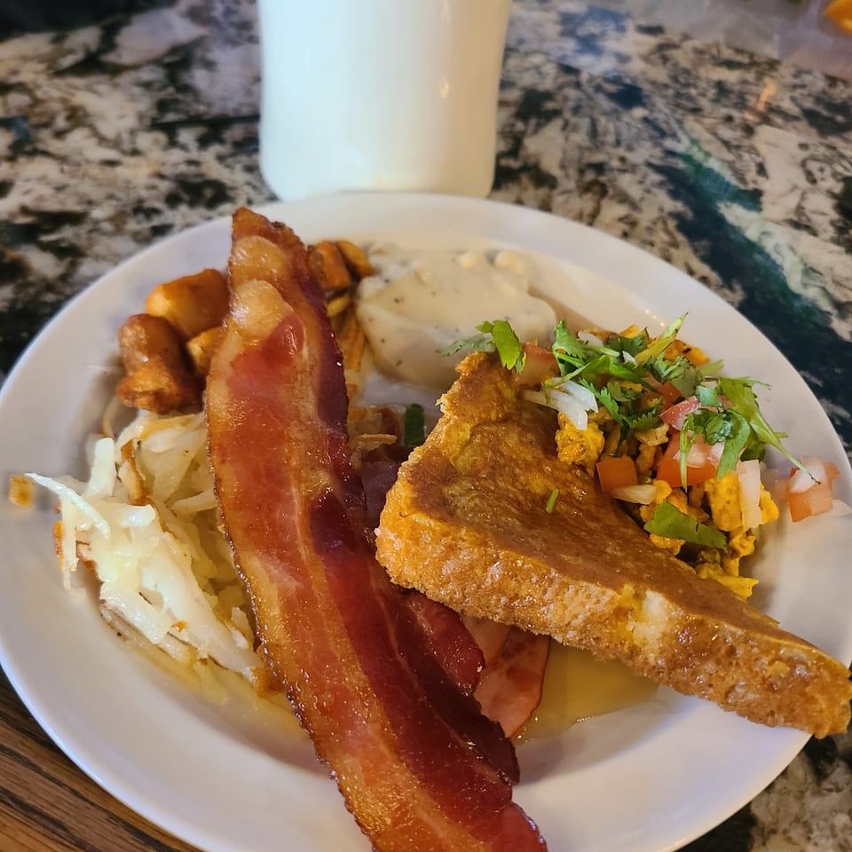 A breakfast plate with bacon, French toast, hash browns, scrambled eggs with salsa, and gravy.