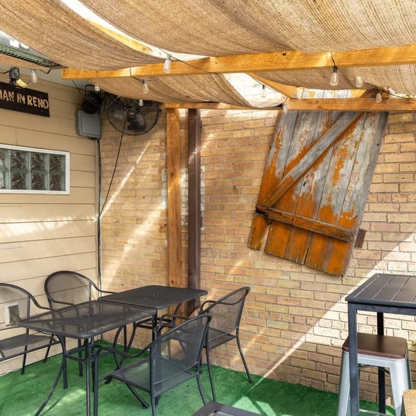 Outdoor patio with black metal tables and chairs, brick wall, and a rustic wooden door decoration.
