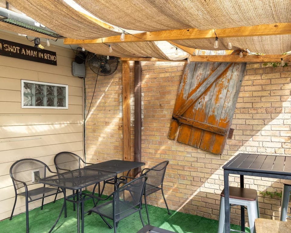 Outdoor patio with black metal tables and chairs, brick wall, and a rustic wooden door decoration.
